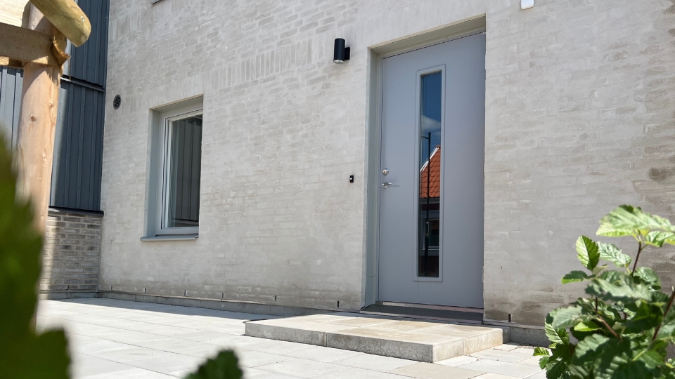 Modern ytterdörr från Dieden-Ekodoor i stilren grå nyans på putsad fasad – svensktillverkad kvalitet med smalt glasparti.