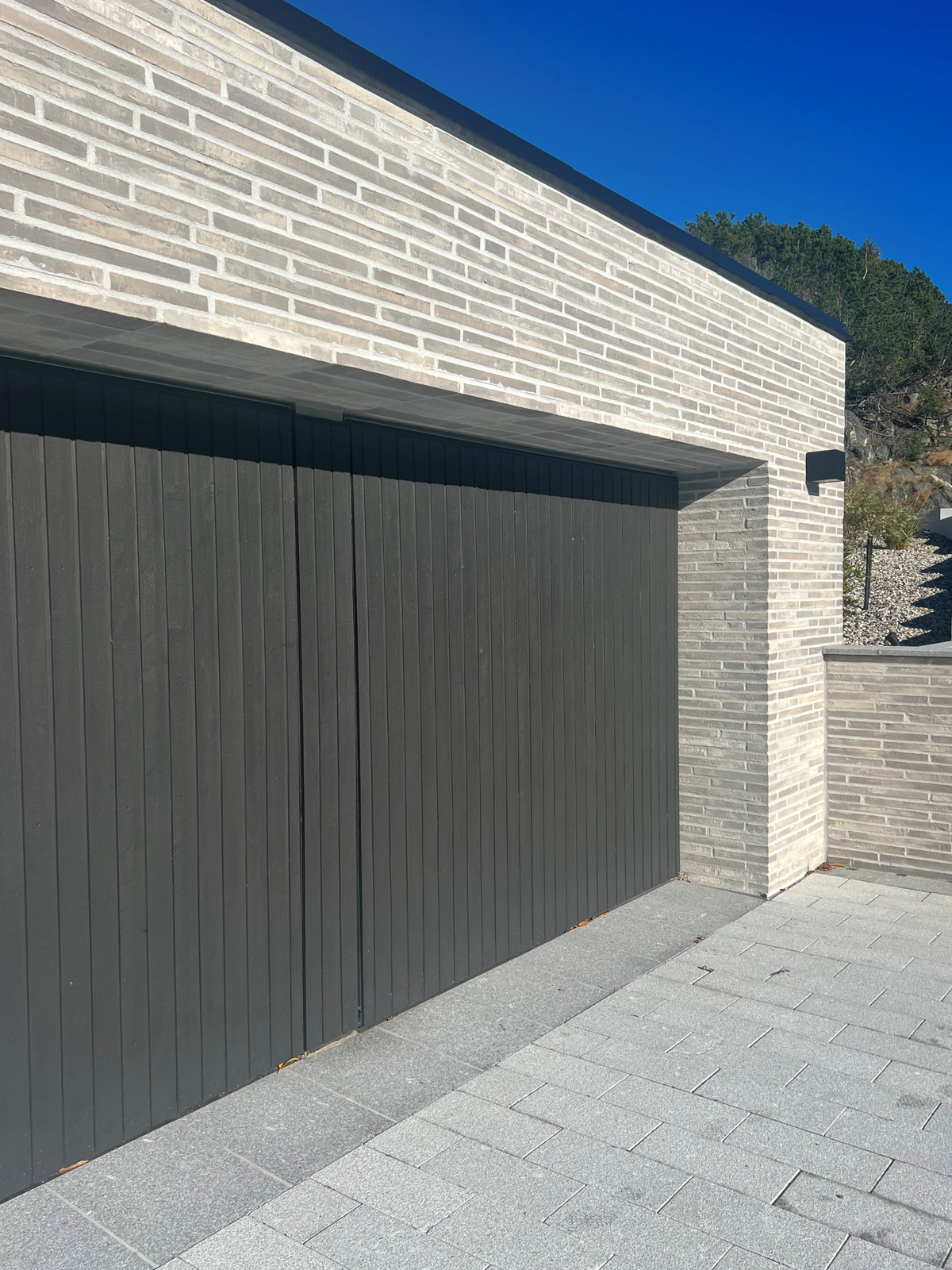 Designport Svart designport från Dieden-Ekodoor med stående trästruktur, integrerad i modern murad garagefasad